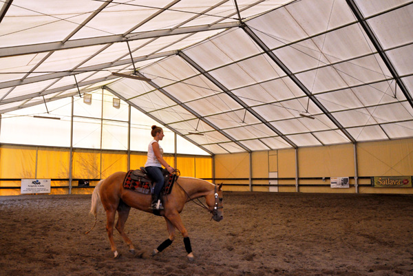 Jezdkyně na koni v plachtové jezdecké hale.