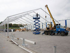 Pracovník pomocí zvedacího zařízení natahuje plachtu na skladovou halu.